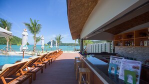 A poolside bar with wooden lounge chairs and a view of the ocean.