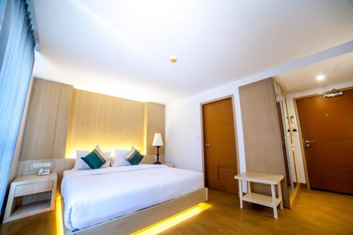A hotel room with a bed, bedside table, lamp, and a small stool.