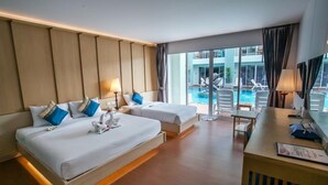 A hotel room with two beds, a desk, and a view of a pool.