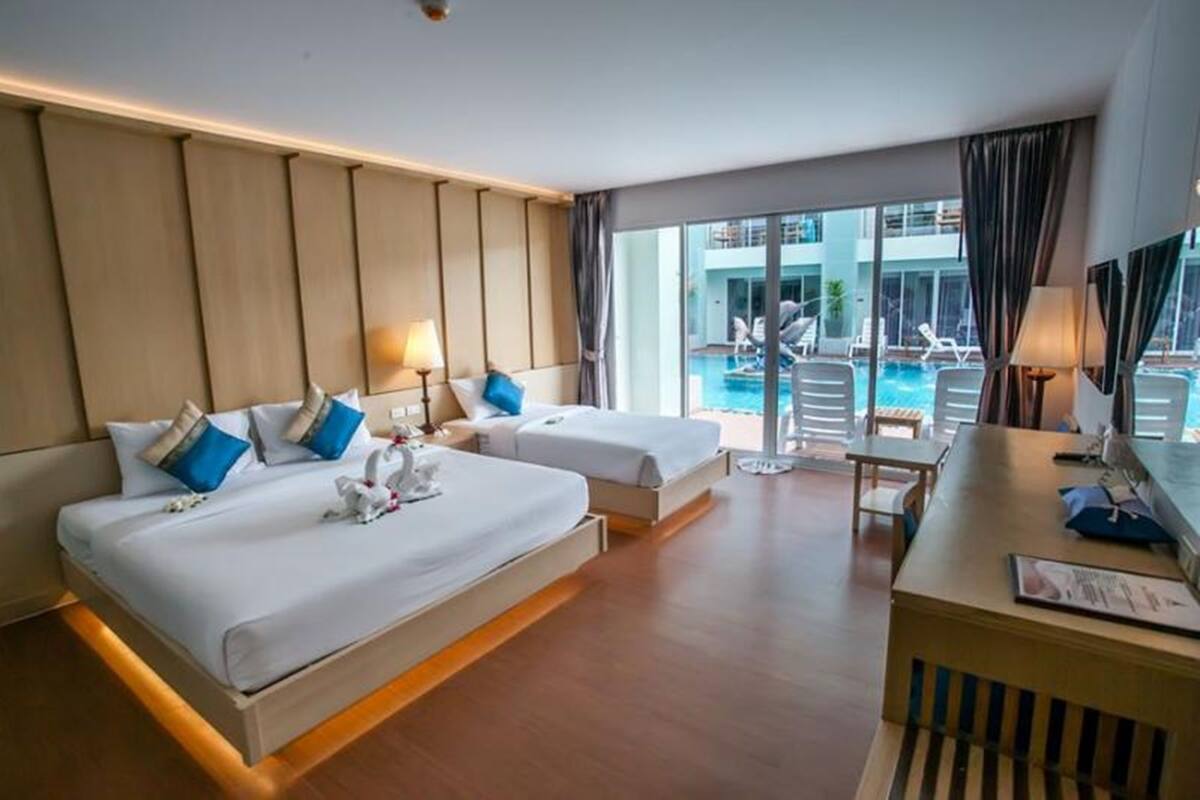 A hotel room with two beds, a desk, and a view of a pool.