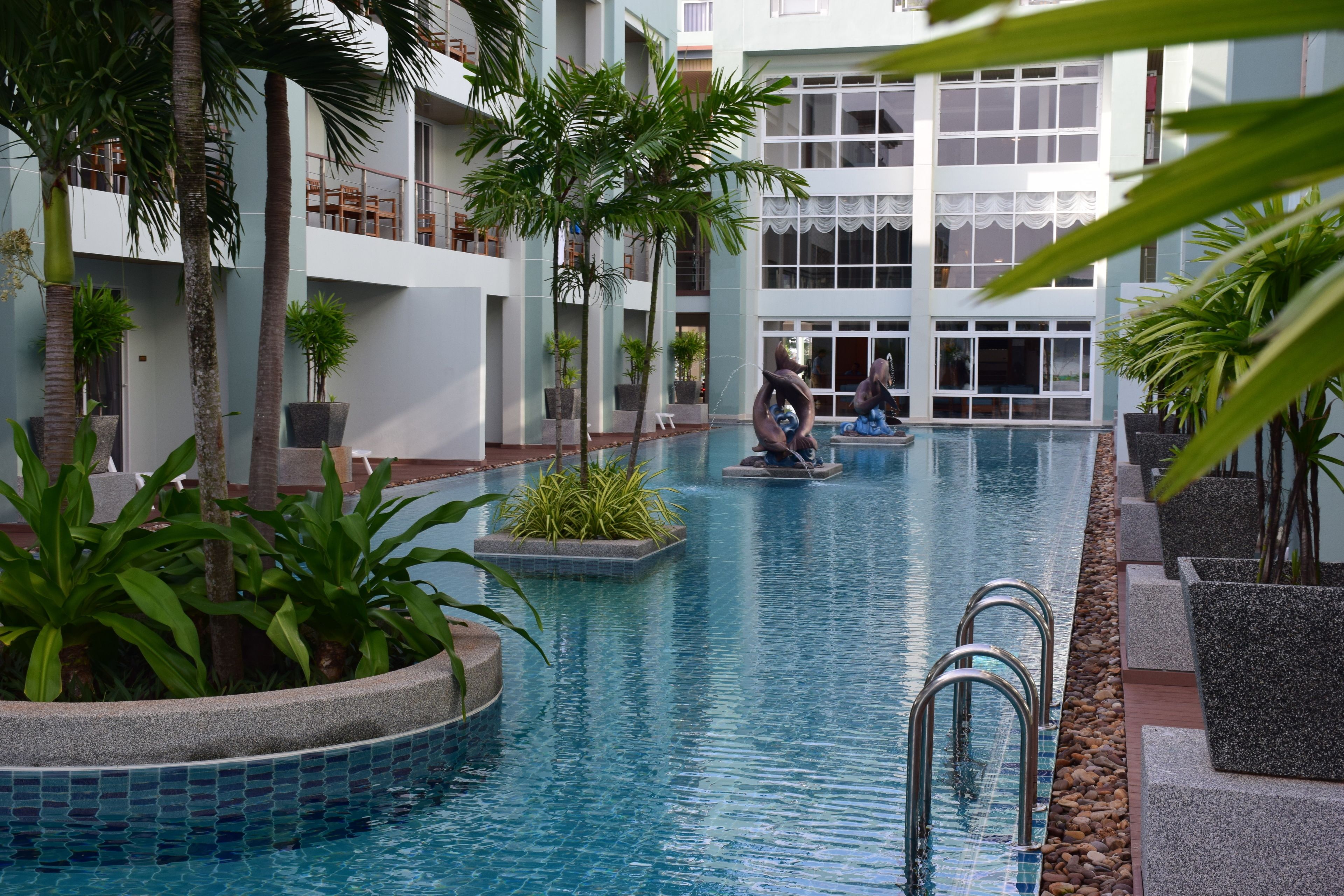 An indoor swimming pool with clear water, surrounded by potted plants and a modern building with balconies.