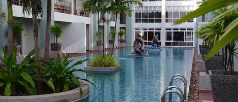 An indoor swimming pool with clear water, surrounded by potted plants and a modern building with balconies.