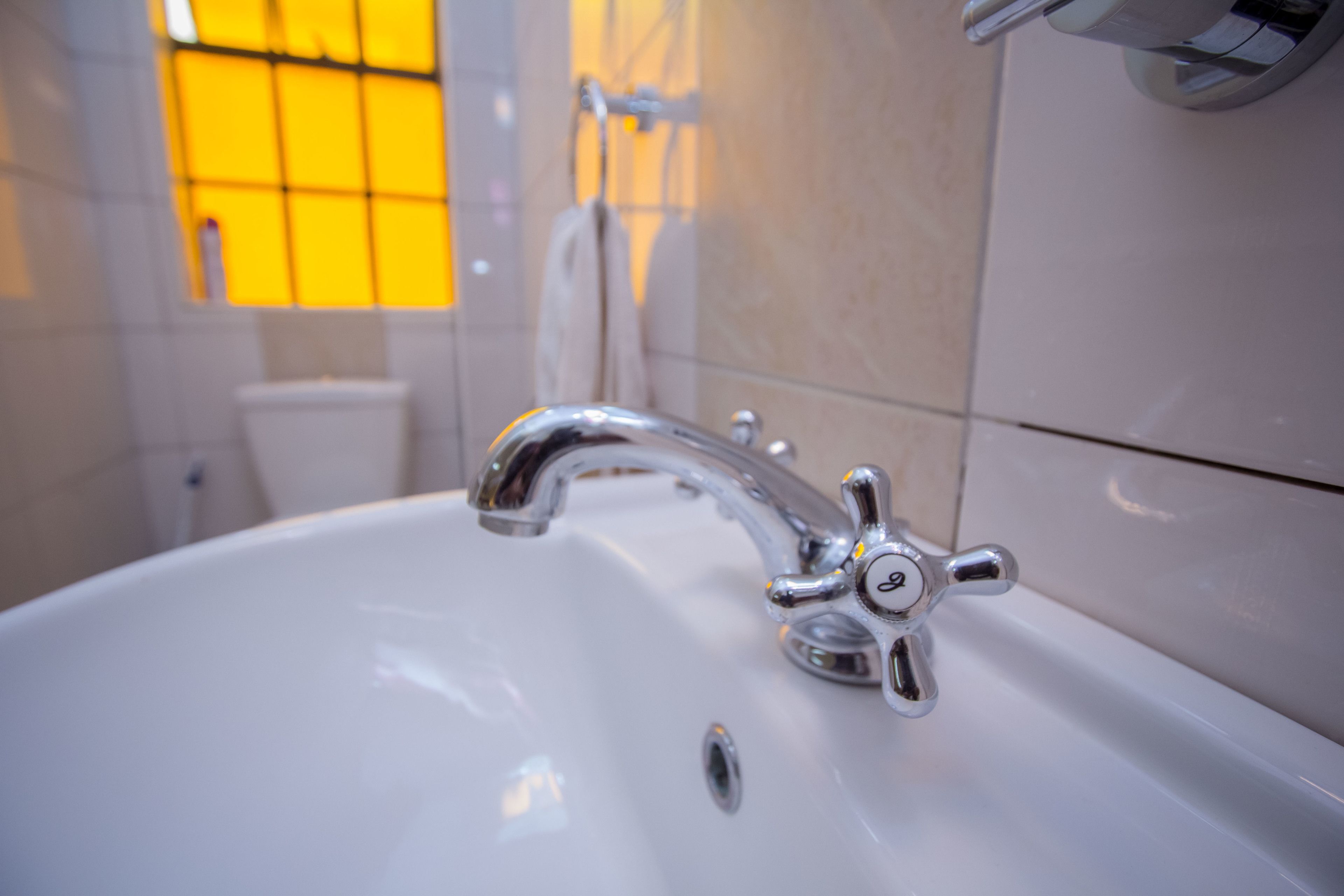 A bathroom sink with a modern faucet, a window with yellow-tinted glass, and a towel rack.