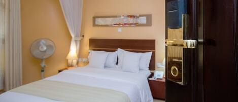 A hotel room with a large bed, a bedside table with a lamp, a wall-mounted artwork, and a door with a keyhole.