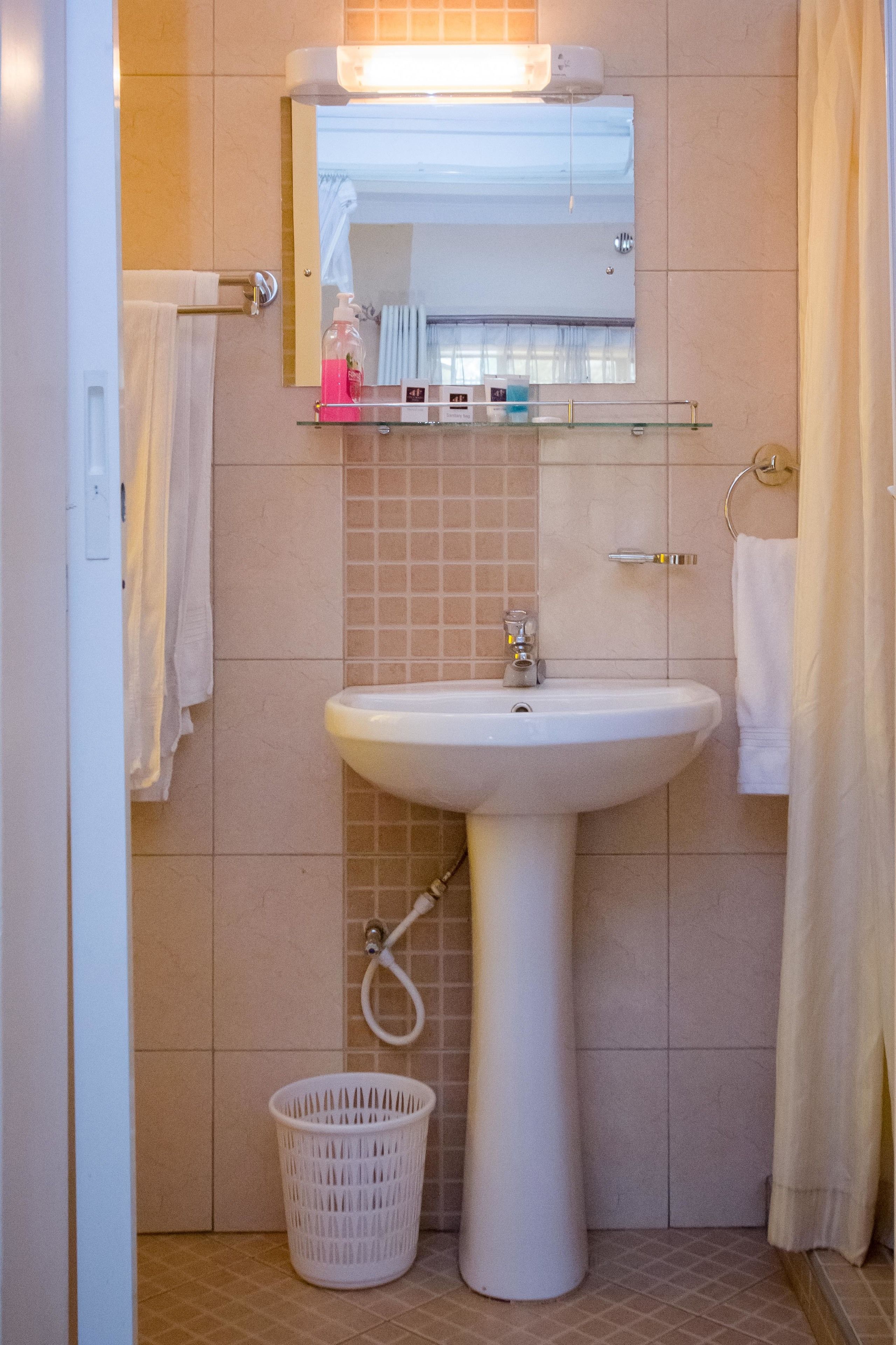 A bathroom with a white sink, a mirror, a glass shelf with toiletries, and a white basket.