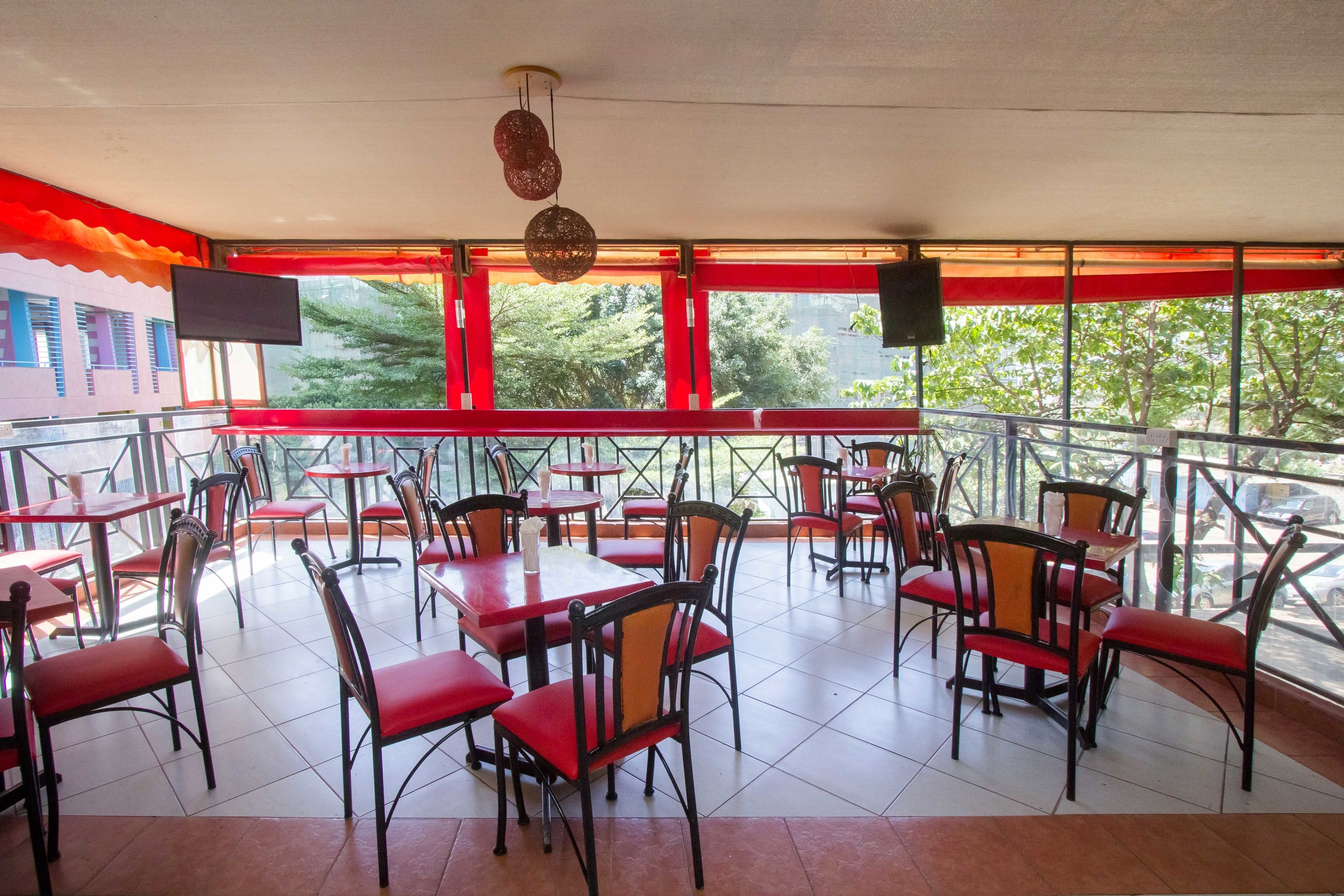 A restaurant with red and black chairs, tables, and a large window with a view of trees.