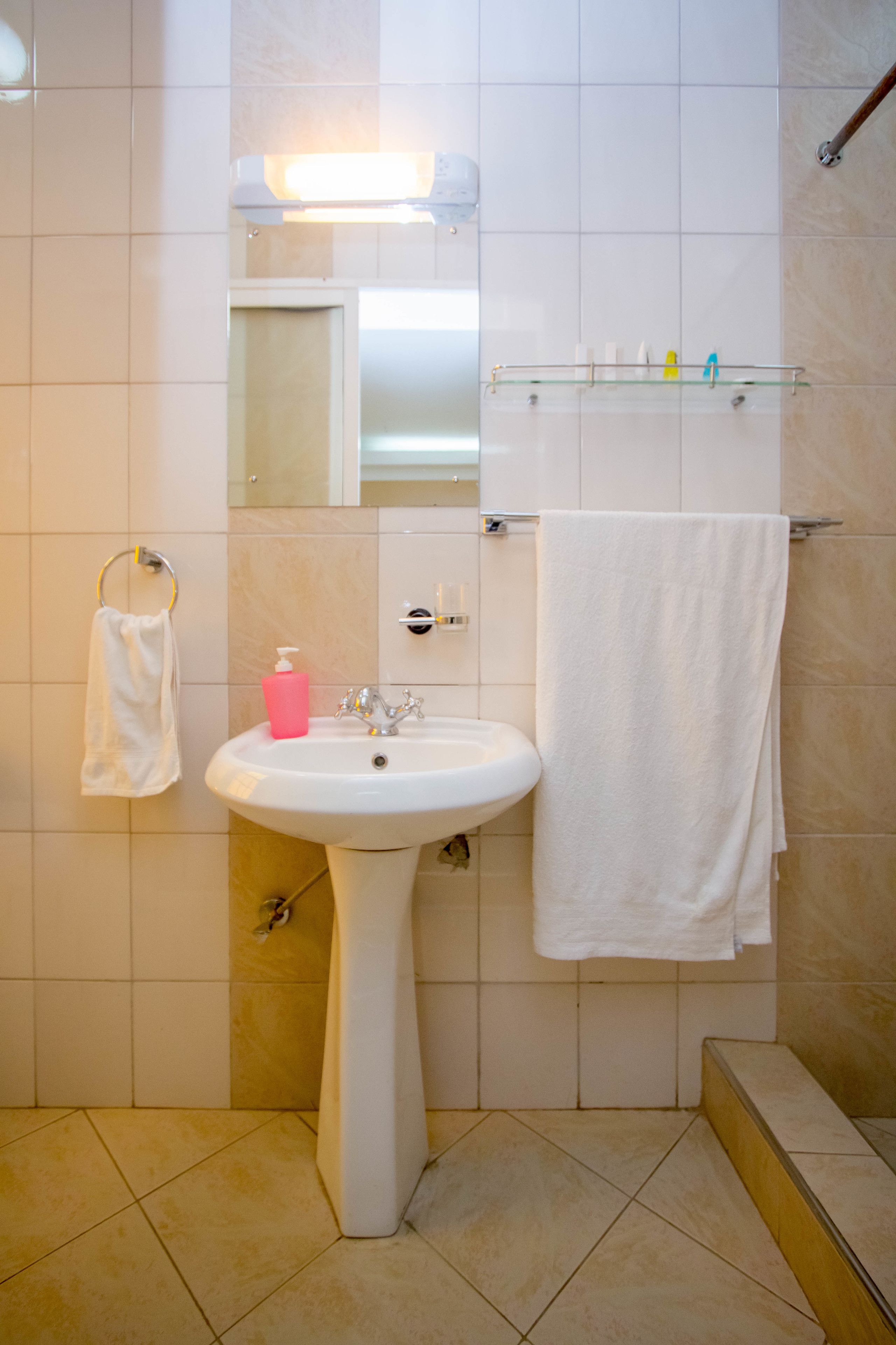 A bathroom with a white sink, a mirror, a towel rack, and a glass shelf with toiletries.