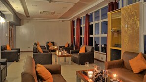 Amplia sala de estar con sofás y sillones de cuero, una mesa de centro con velas y grandes ventanales con cortinas.