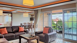 Una sala moderna con un sofá, sillones y una mesa de centro. Hay un comedor con sillas y una mesa. Grandes ventanales ofrecen vistas al exterior.