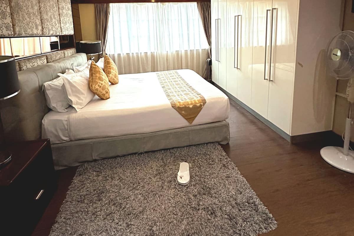 A modern bedroom with a large bed, a standing fan, and a wardrobe.