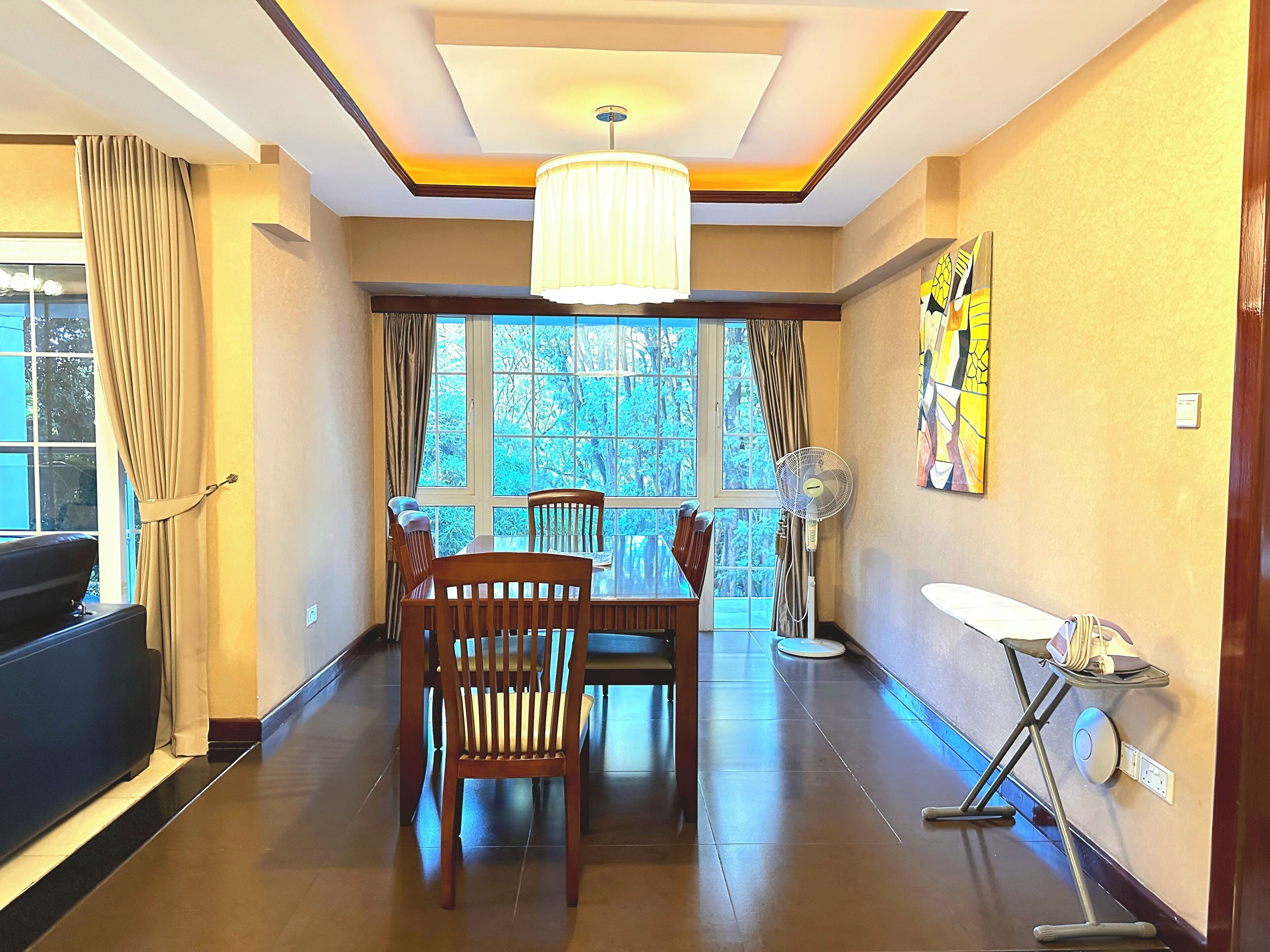 A dining area with a table and chairs, a standing fan, and a ceiling light fixture.
