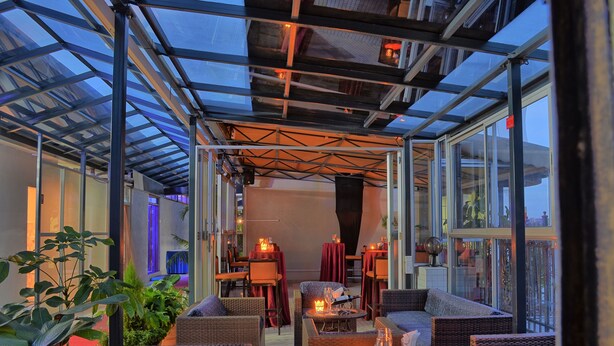 Un patio al aire libre con mobiliario de mimbre, mesas de vidrio e iluminación ambiental.