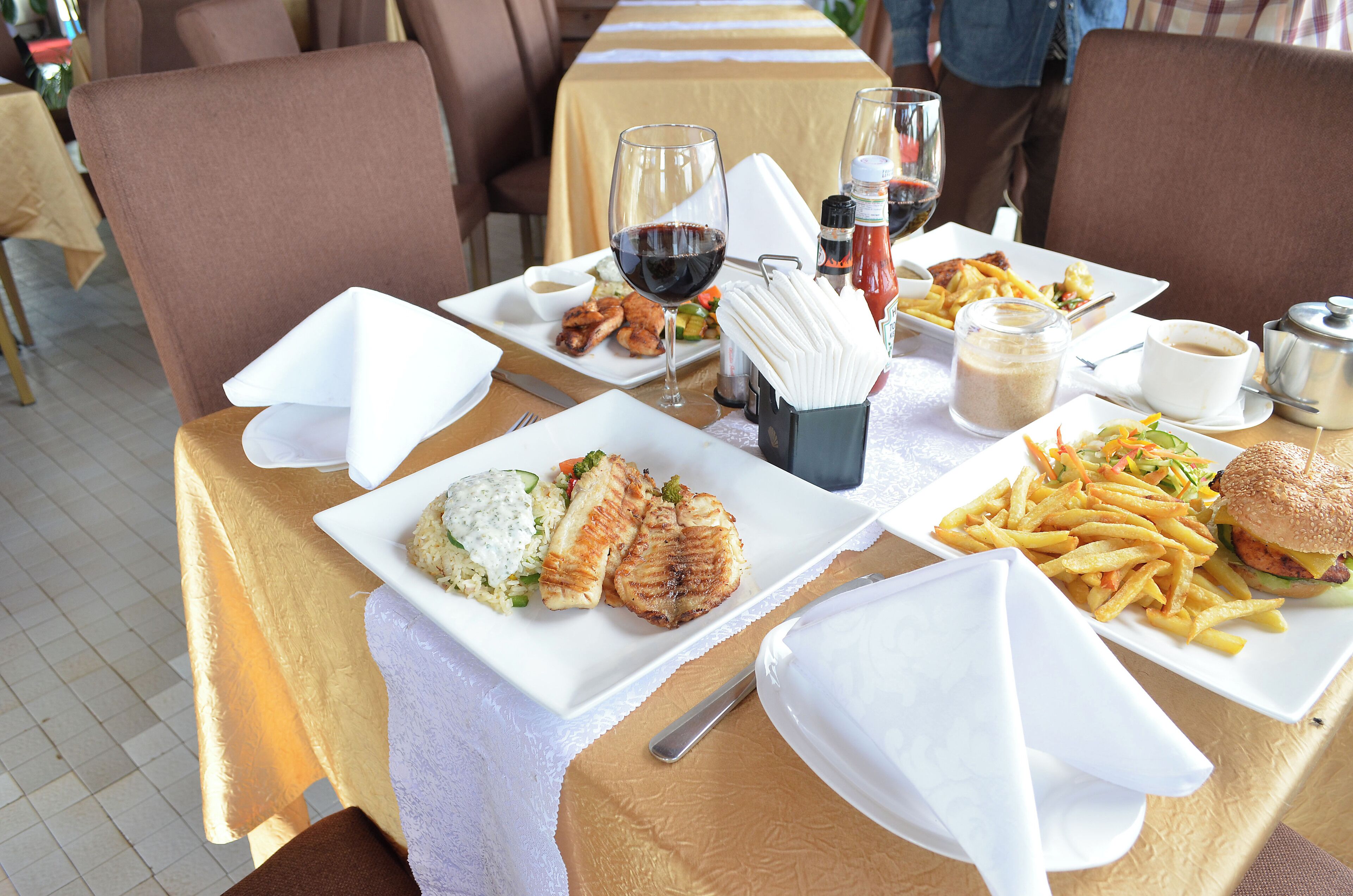 Una mesa de comedor con platos de comida, una copa de vino y aderezos.
