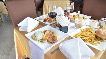 Una mesa de comedor con platos de comida, una copa de vino y aderezos.