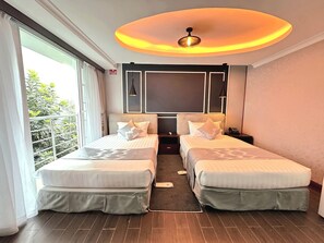 Een hotelkamer met twee bedden, een groot raam, een plafondlamp en uitzicht op groen.