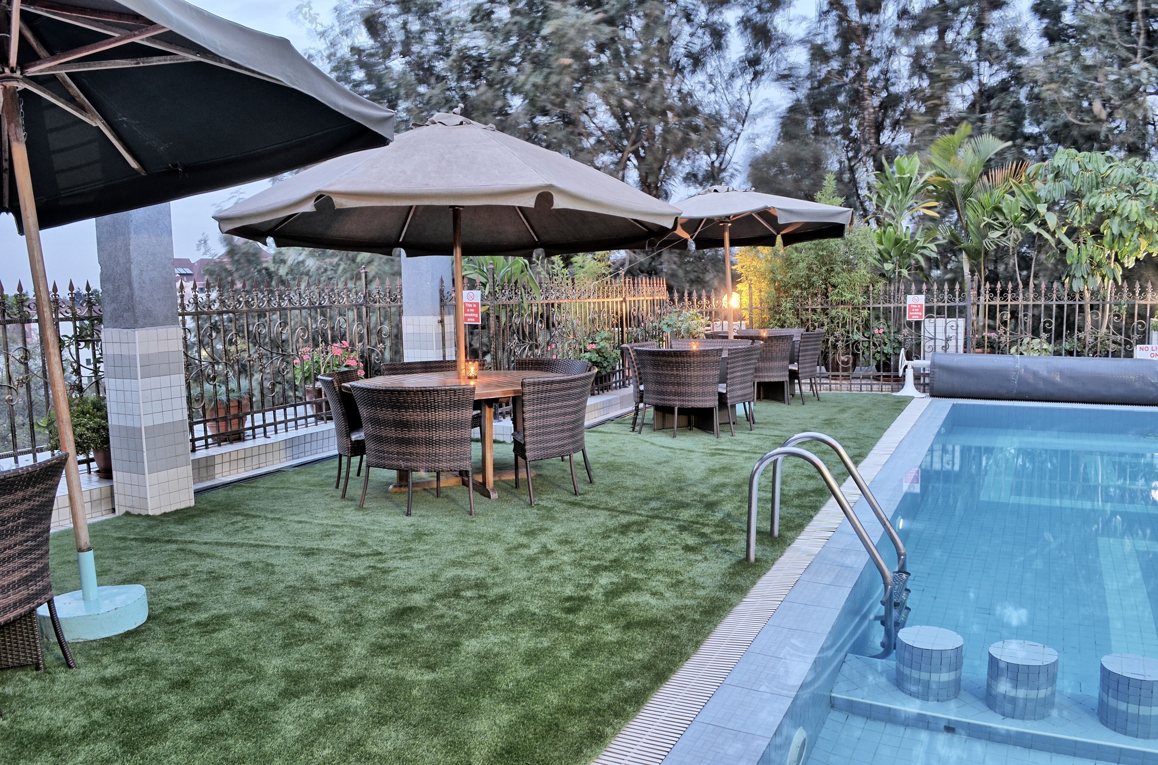An outdoor pool area with artificial grass, wicker furniture, and umbrellas.