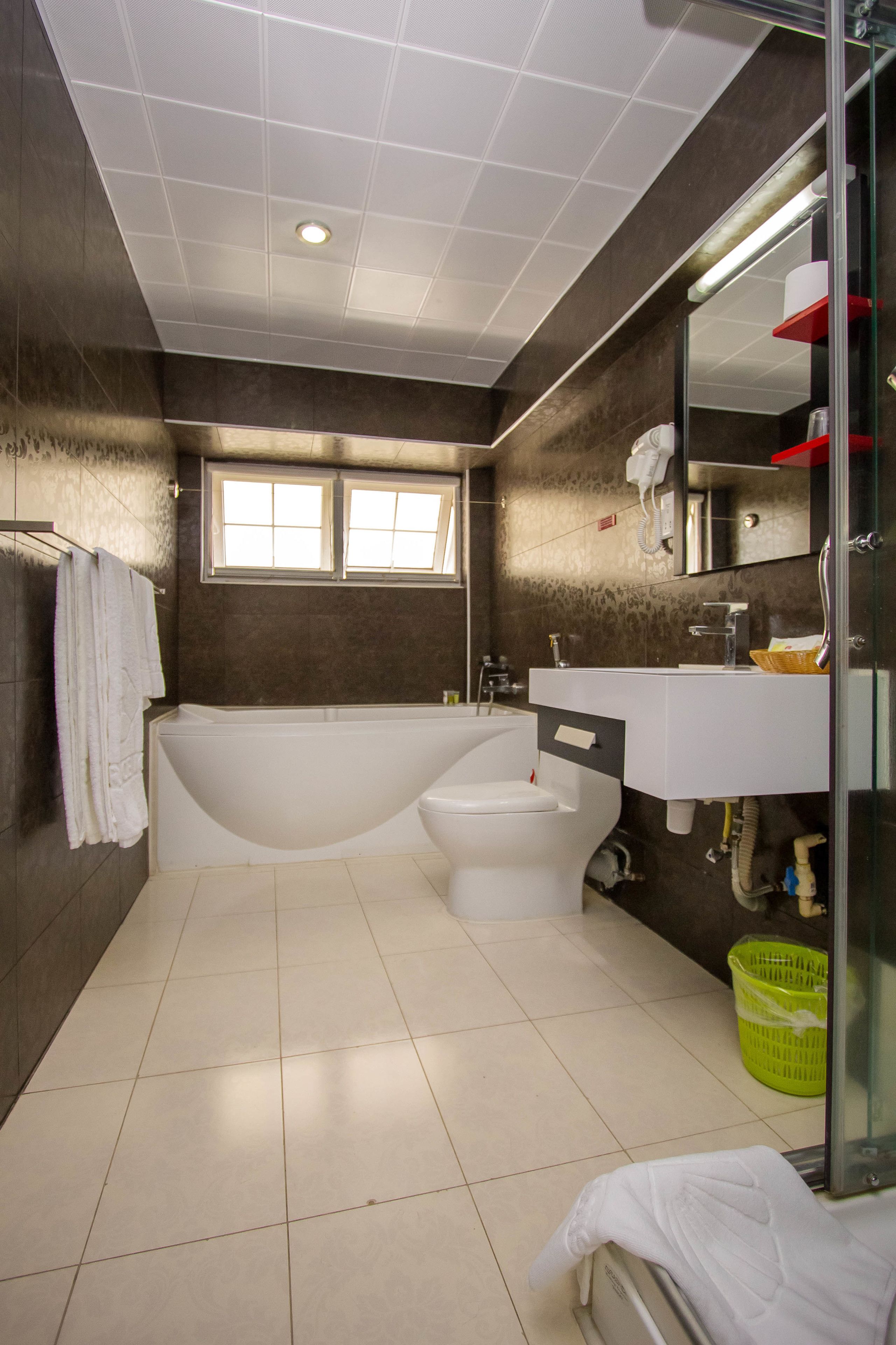 Un baño moderno con bañera, inodoro y lavamanos. Hay una ventana que proporciona luz natural y un espejo sobre el lavamanos.