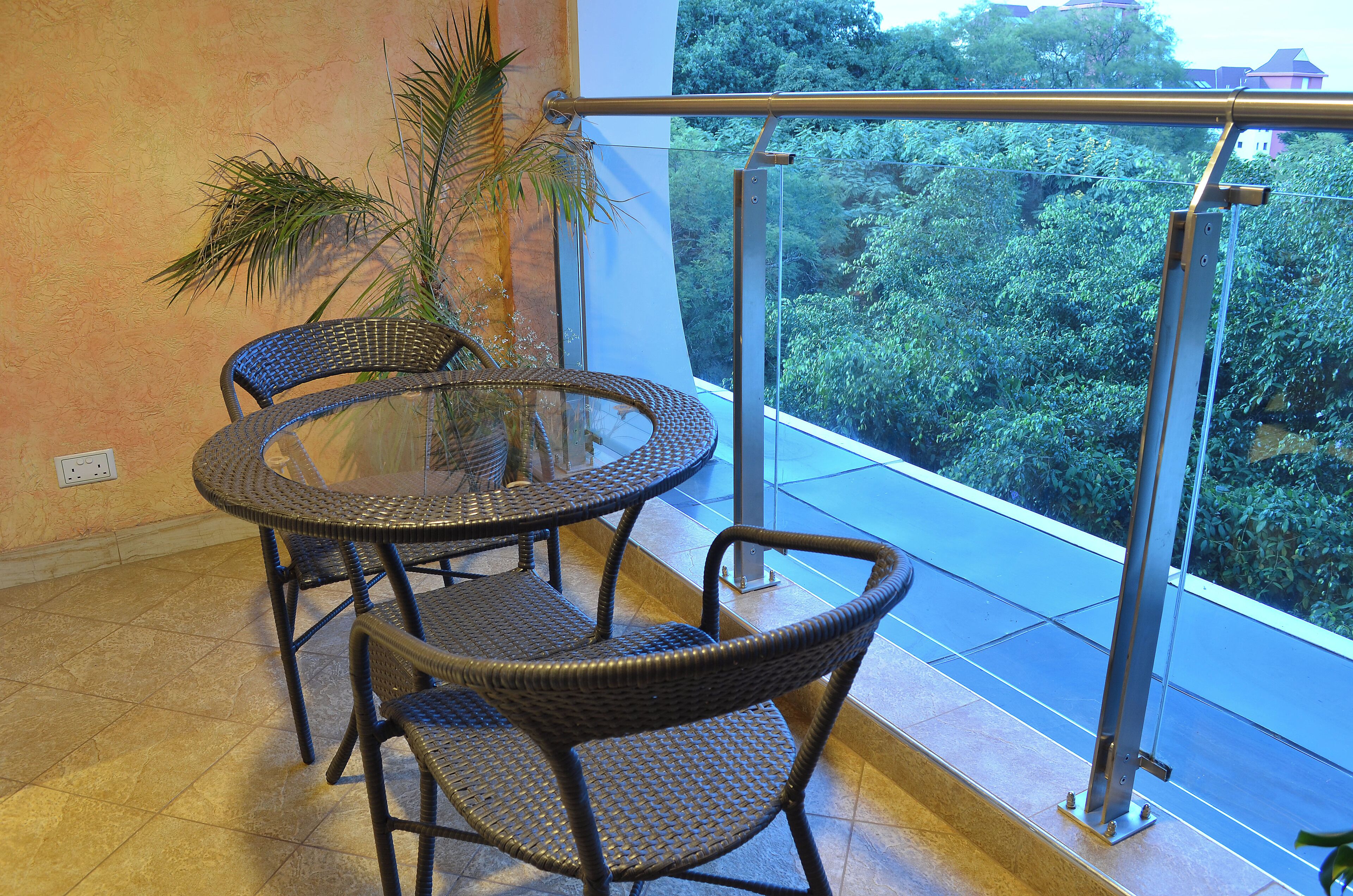 A balcony with wicker furniture and a glass table, overlooking a lush green landscape.