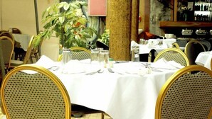 Un espace repas avec des tables rondes disposées pour accueillir quatre personnes, chacune étant recouverte d’une nappe blanche, entourée de chaises dorées et agrémentée d’une plante en pot au centre.