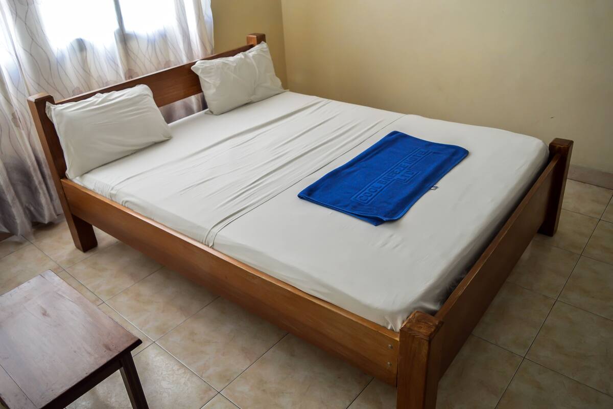 Een eenpersoonsbed met houten frame, witte beddengoed en een blauwe handdoek.