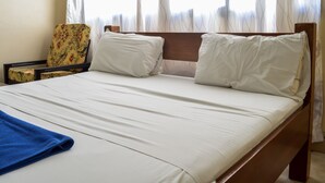 Una cama bien hecha con sábanas blancas, una toalla azul y un cabecero de madera.