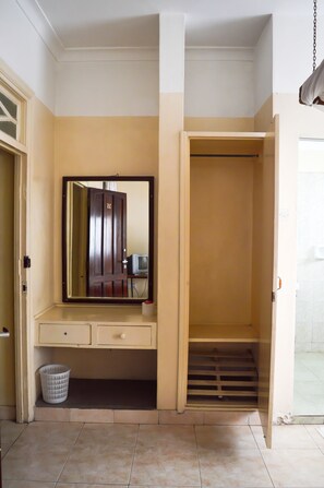 A room with a large mirror, a wardrobe, a small trash bin, and a tiled floor.