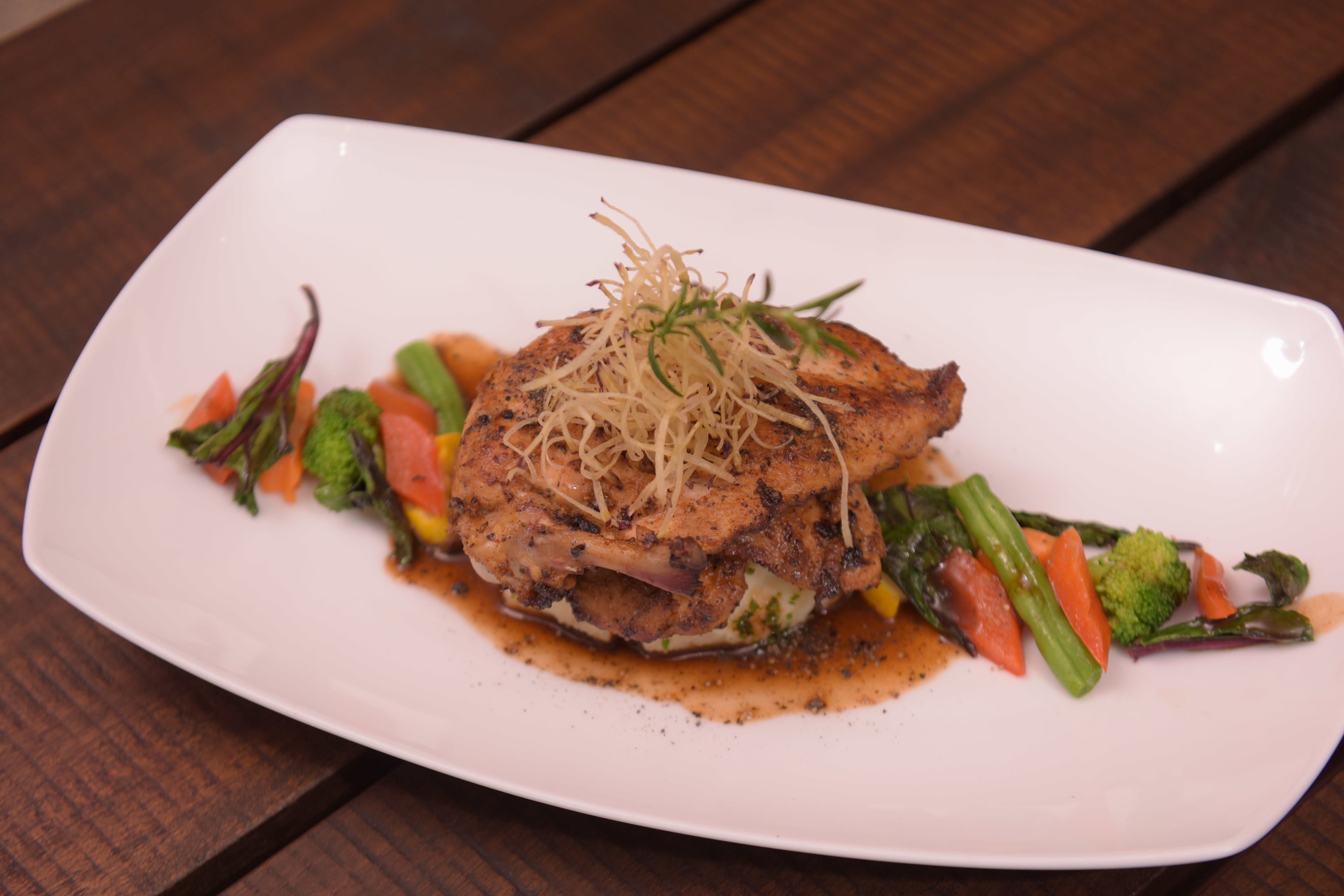 A white plate with a grilled chicken breast, asparagus, and carrots.