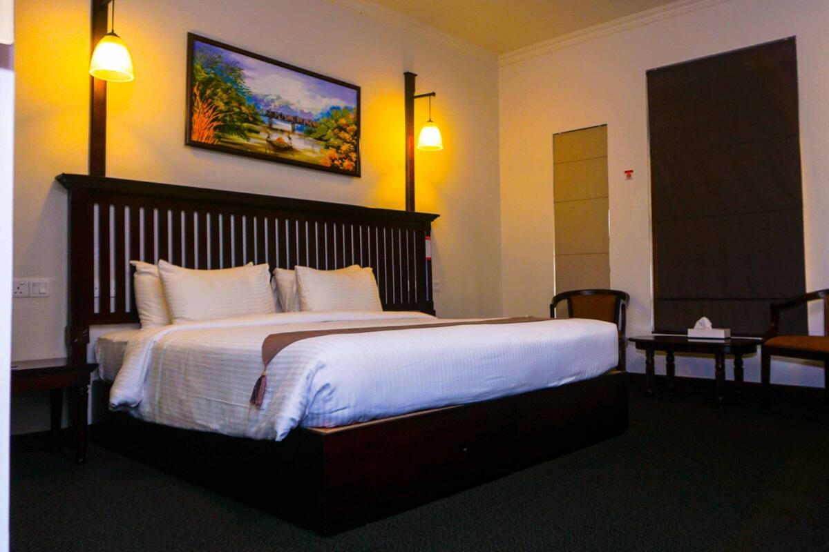 A hotel room with a large bed, two chairs, a small table, and a painting on the wall.