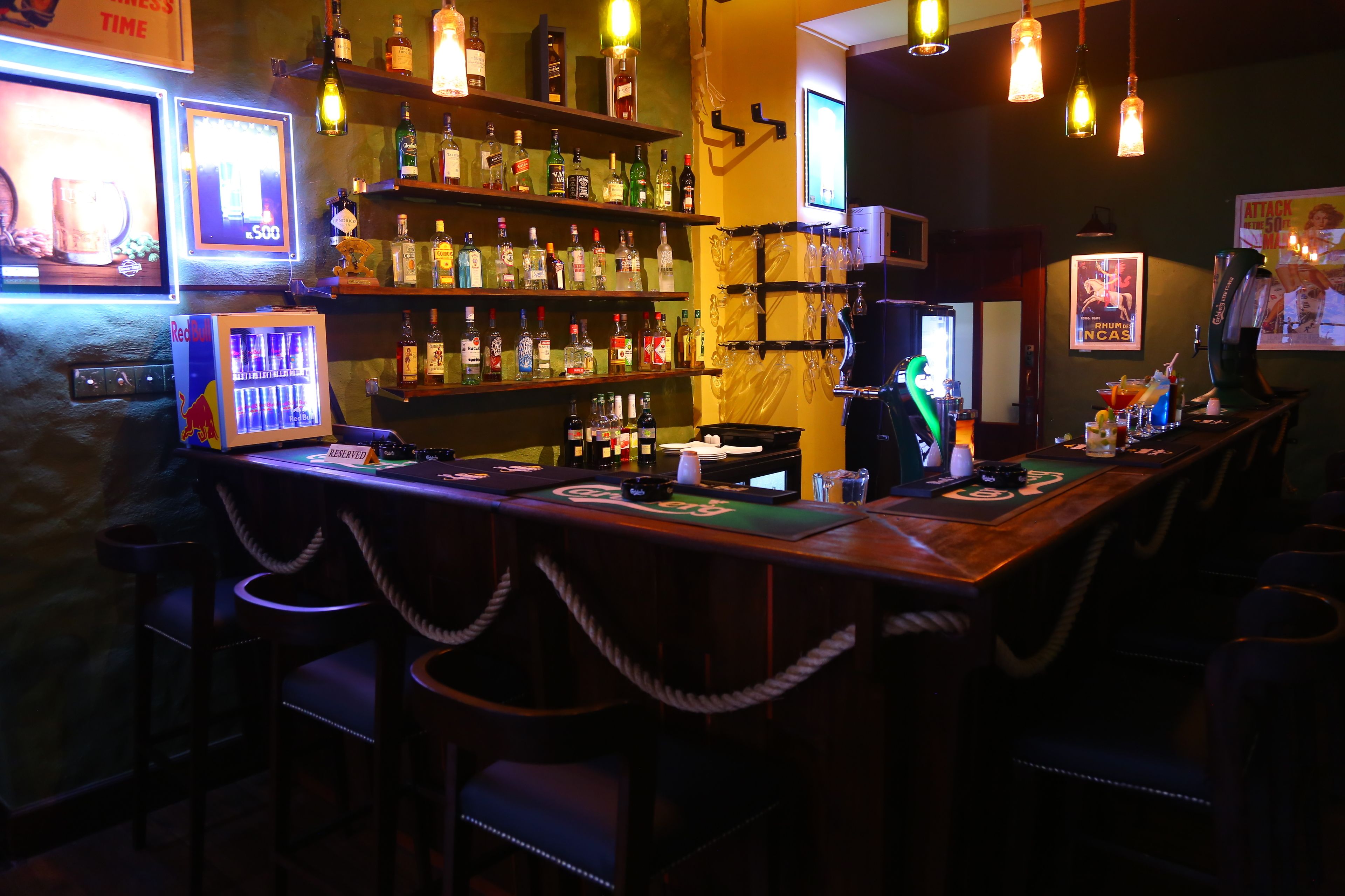 Een bar met verschillende drankflessen, een televisie en een bar met krukken.