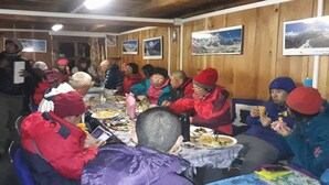 A group of people seated around a table in a wooden room with framed pictures on the walls. - 8000 Inn (Lobuche)