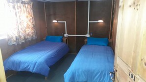 A room with two beds, each with a blue bedspread and matching pillows, and a curtain on the window. - 8000 Inn (Lobuche)