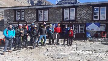A group of people standing in front of a stone building with windows and a signboard.