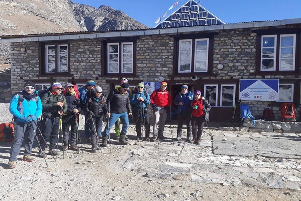 A group of people standing in front of a stone building with windows and a signboard.