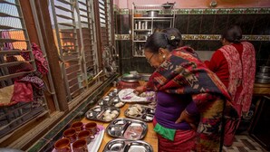 Uma cozinha com bandejas e utensílios de metal, uma janela com grades e um painel de azulejos.