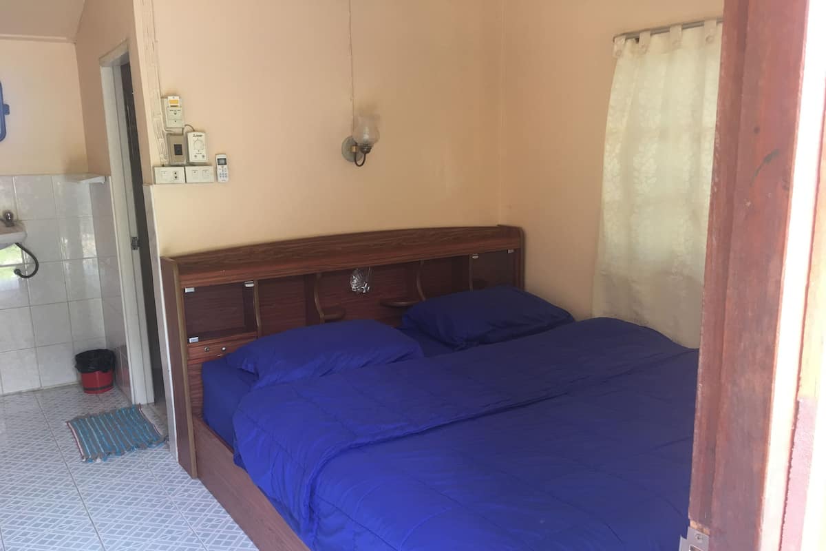 Un dormitorio con cabecera de madera, colcha azul, lámpara de pared y suelo de baldosas.