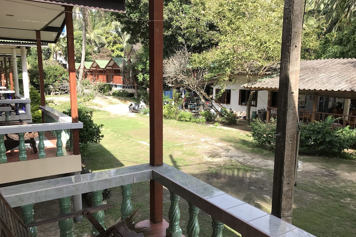 Un espacio al aire libre cubierto con vista a un jardín y un edificio al fondo.
