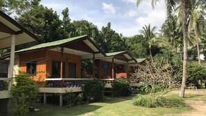 A row of wooden cabins with green roofs, surrounded by lush greenery and palm trees. - Blue Lotus Resort (Ko Pha-ngan)