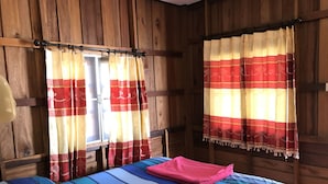 A wooden cabin room with a bed, two windows with curtains, and a wooden headboard. - Blue Lotus Resort (Ko Pha-ngan)