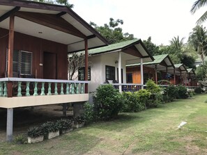 A row of wooden cabins with green roofs, white railings, and a well-maintained lawn.
