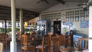 A restaurant with wooden tables and chairs, a refrigerator, and a counter with various items. - Blue Lotus Resort (Ko Pha-ngan)