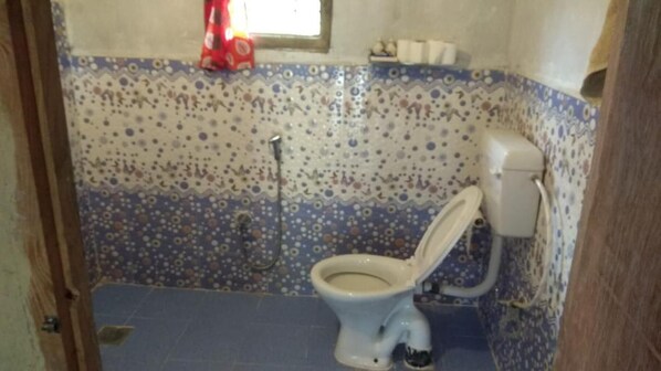 A bathroom with a toilet, a shower, and a patterned wall. - Barauli Community Homestay (Kawasoti)