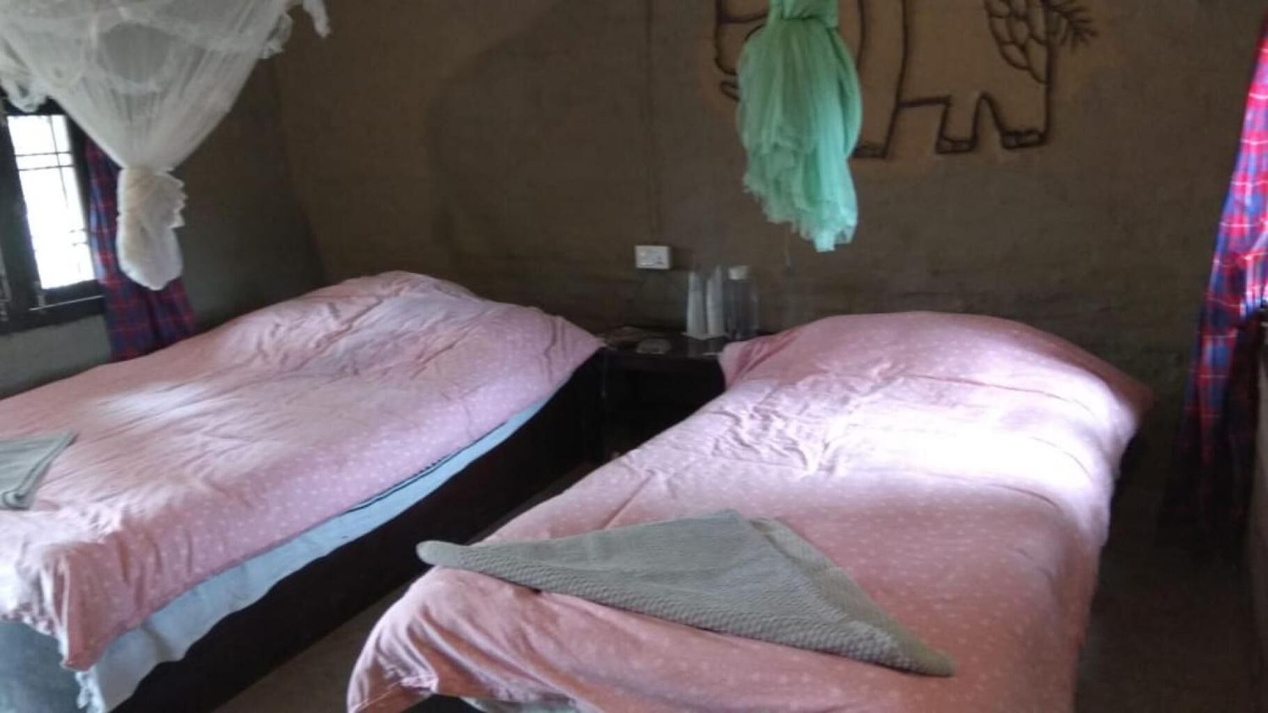Een kamer met twee bedden, elk met een roze dekbedovertrek en een groen sierkussen. Er hangt een muggengaas aan het plafond.