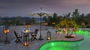 Un espacio de comedor al aire libre con una mesa y sillas, rodeado de faroles y una piscina pequeña con iluminación verde.