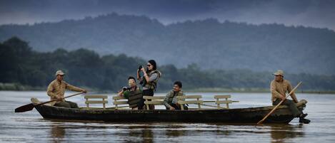 A rowboat with four people, one taking a photo, on a calm body of water with mountains in the background.
