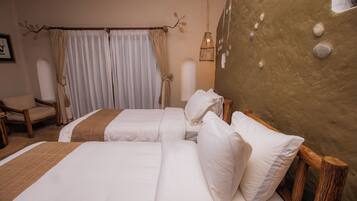 Quarto de hotel com duas camas, uma cadeira, uma janela grande com cortinas e uma parede com textura diferenciada.