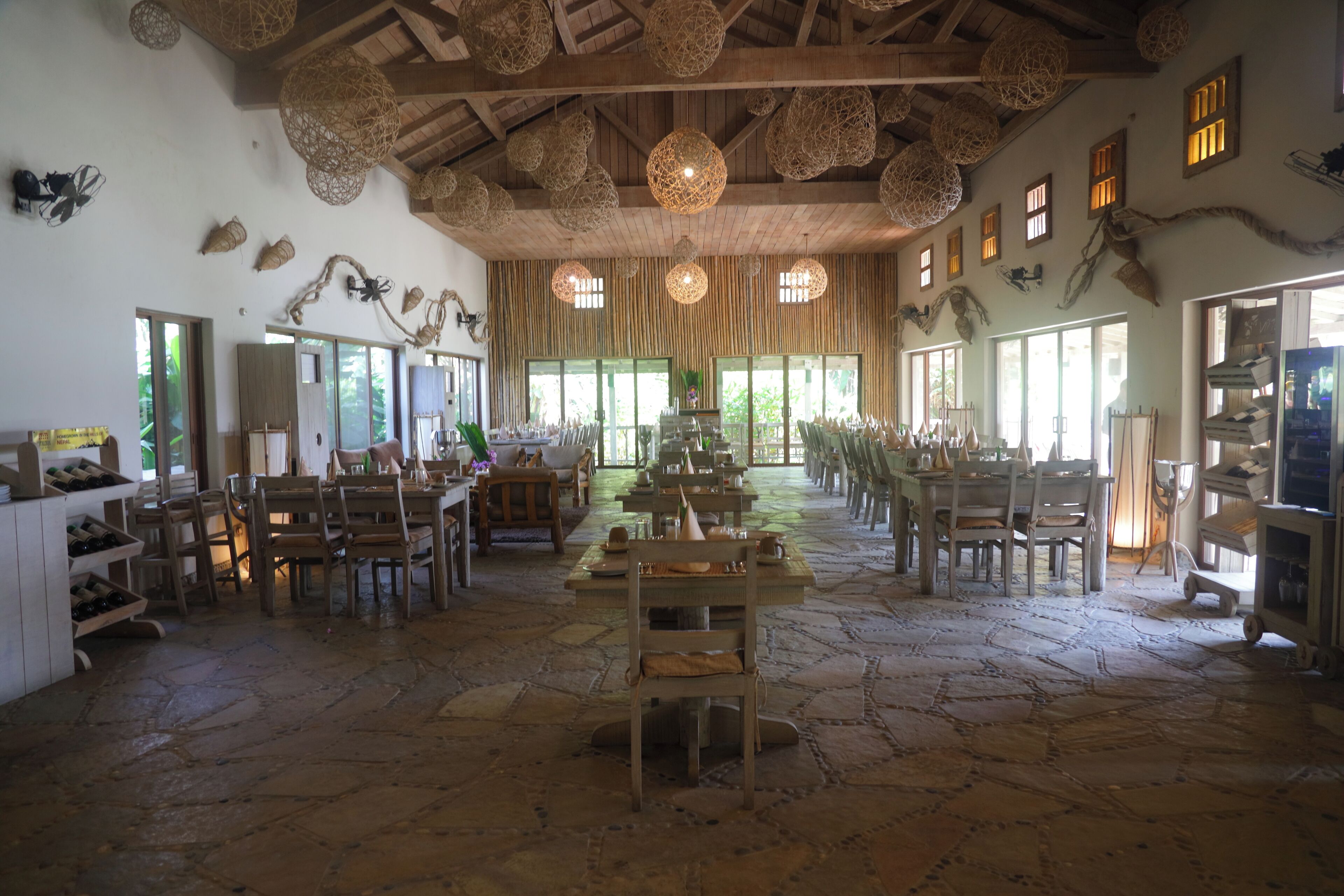 A spacious room with stone flooring, wooden furniture, and a high ceiling with woven light fixtures.