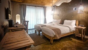 Un dormitorio rústico con dos camas, una mesa de madera, una silla y un ventanal con cortinas.