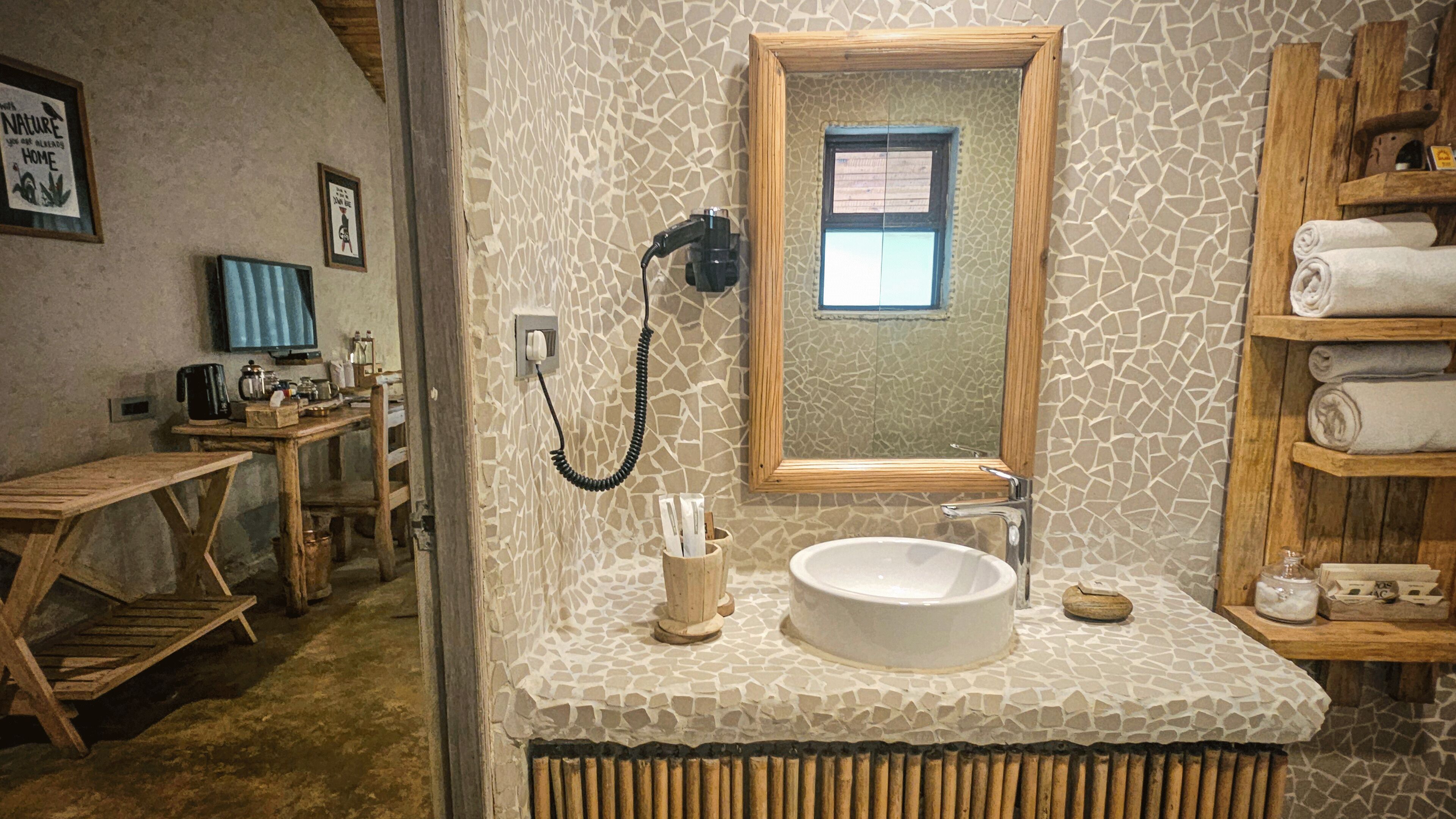 Ein Badezimmer mit Fliesenrückwand aus Stein, einem spiegel mit Holzrahmen, einem Waschbecken und einem Handtuchhalter.
