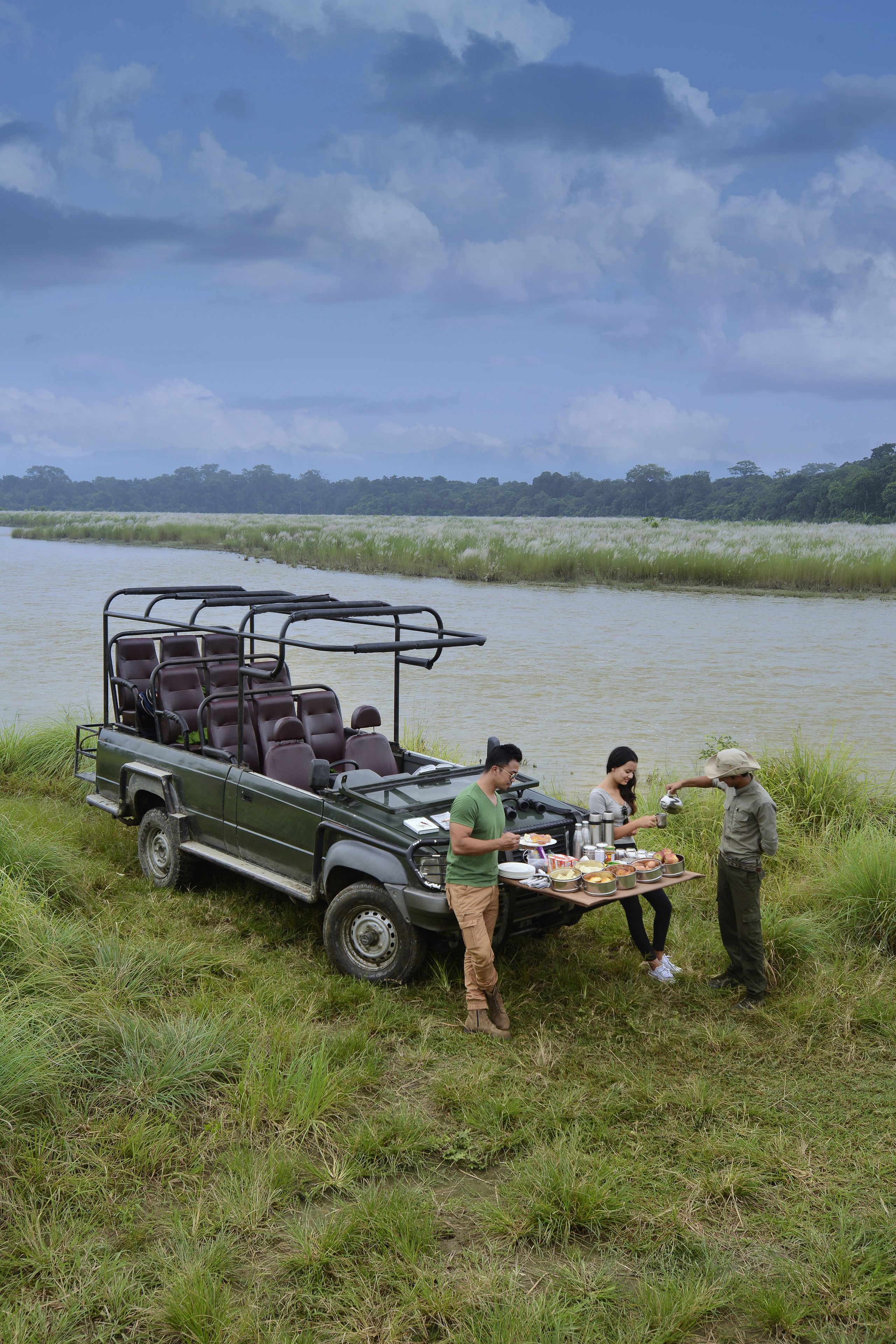 Un véhicule de safari est garé près d’une rivière, et des personnes préparent de la nourriture.