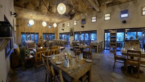 Un comedor rústico con mesas y sillas de madera, ventanas amplias y lámparas colgantes.
